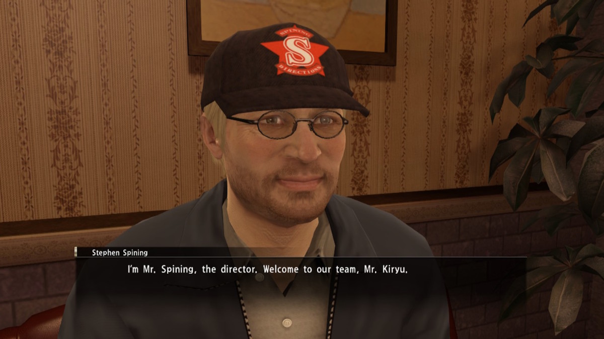 An animated man meant to look like Stephen Spielberg is sitting on a chair in a dimly lit cafe